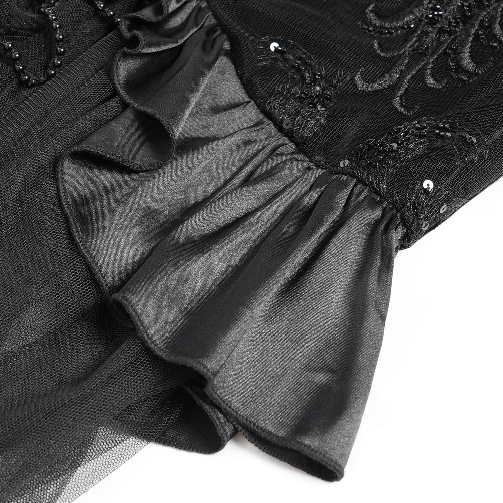 Close-up of gothic black velvet dress featuring intricate beadwork and sheer ruffle hemline for elegant evening wear.