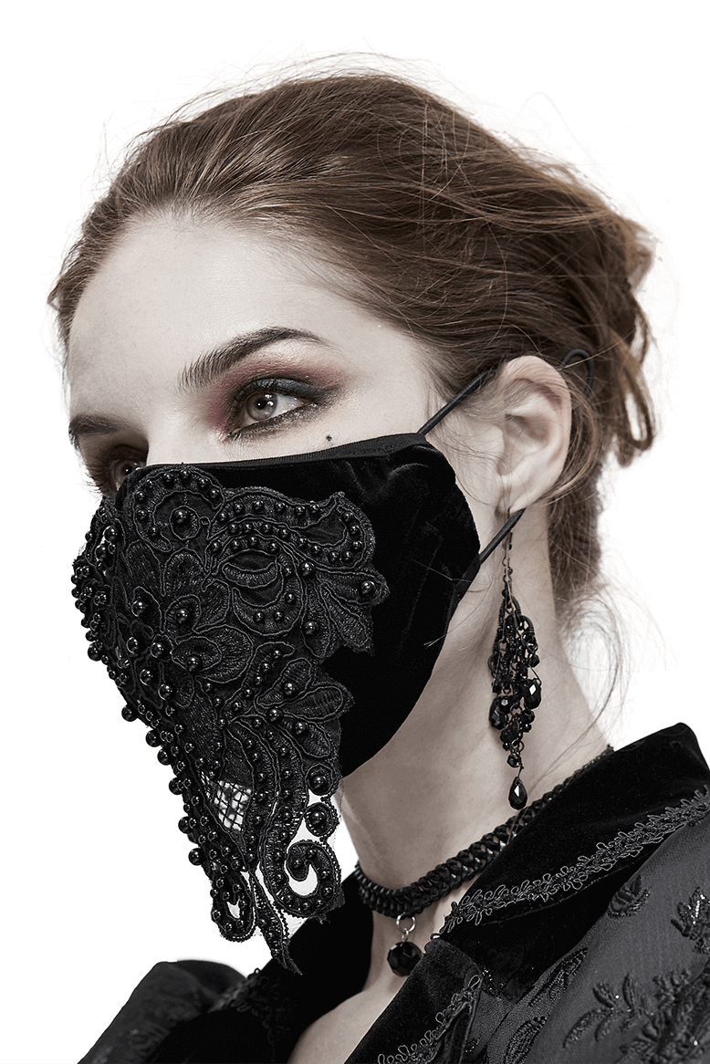 Gothic black velvet mask with lace applique and adjustable straps, worn by a model with elegant accessories.