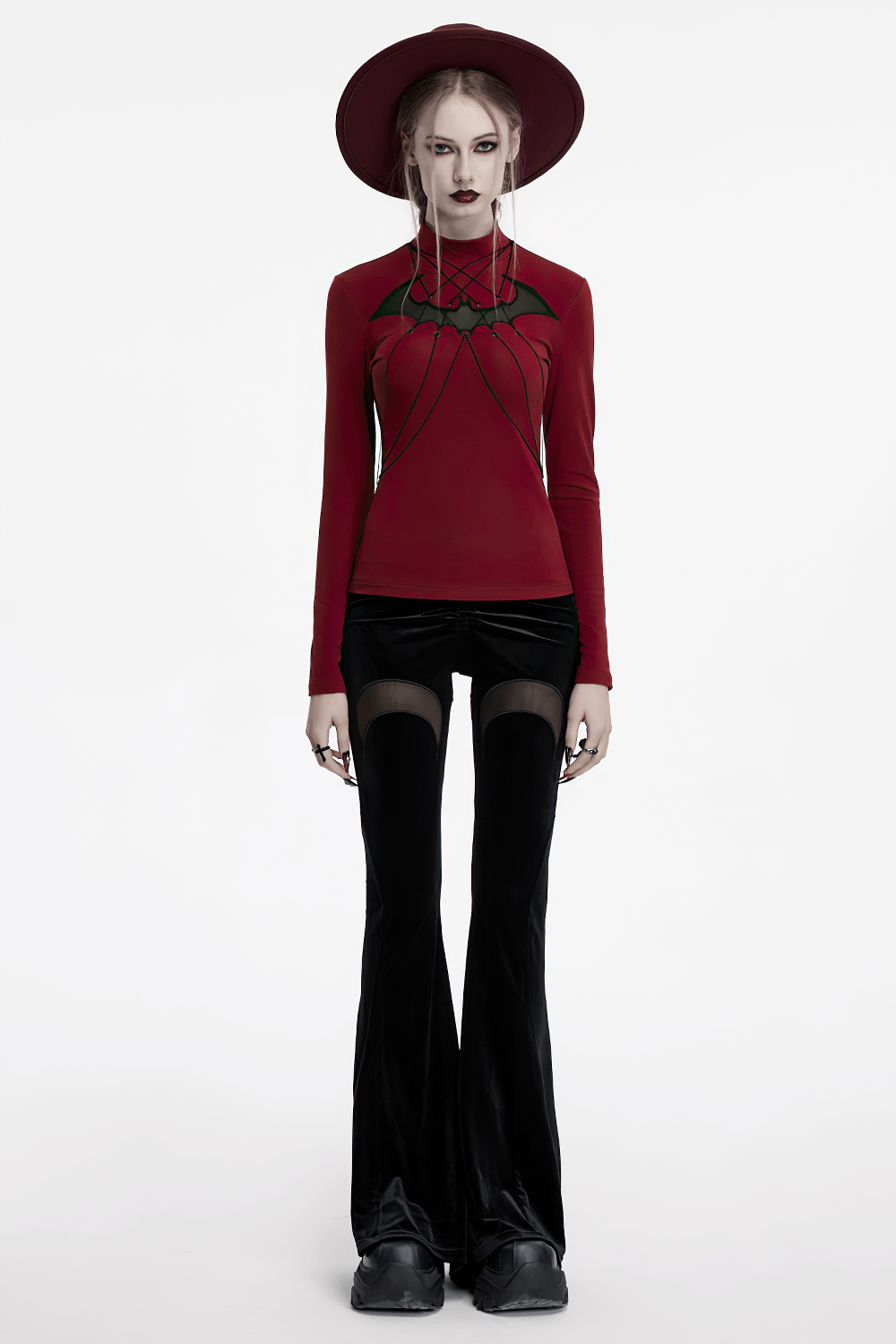 Gothic black velvet flared pants with mesh cutouts, paired with a red top and hat for a witchy streetwear look.