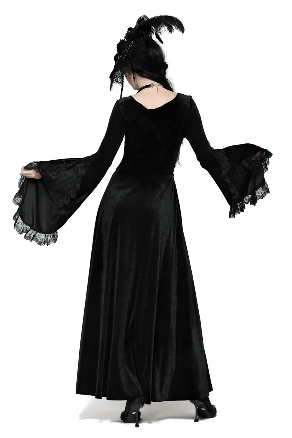 Elegant woman in a gothic black velvet dress with bell sleeves and lace details, showcasing a flowing skirt and a dramatic look.