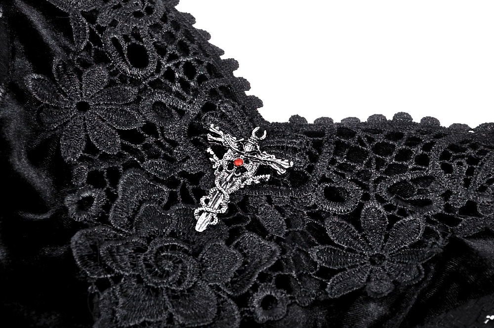 Close-up of intricate lace and gothic pendant on a black velvet dress, featuring floral embroidery and dark elegance.