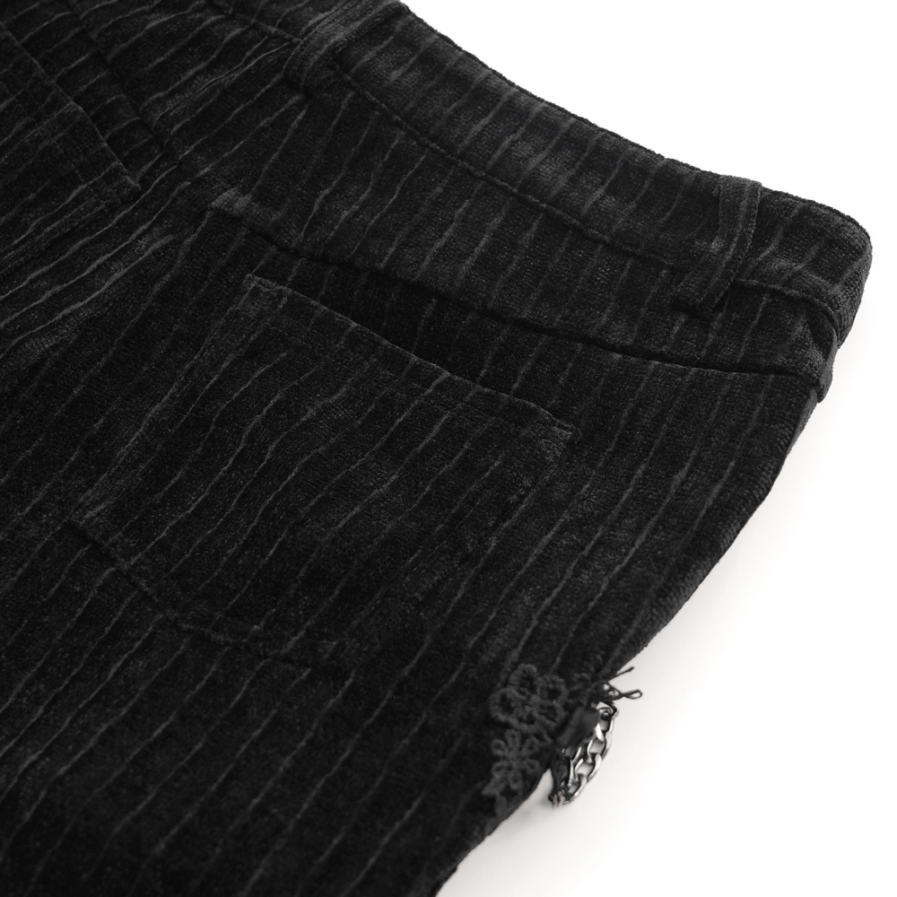 Close-up of gothic black velvet slim fit pants showcasing embroidered detail and chain embellishments on a textured background.