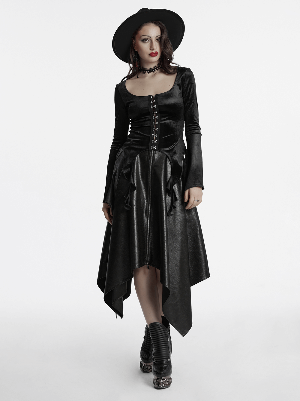 Gothic black velvet top with square collar, metal buckles, and flowing skirt, accessorized with a stylish hat.