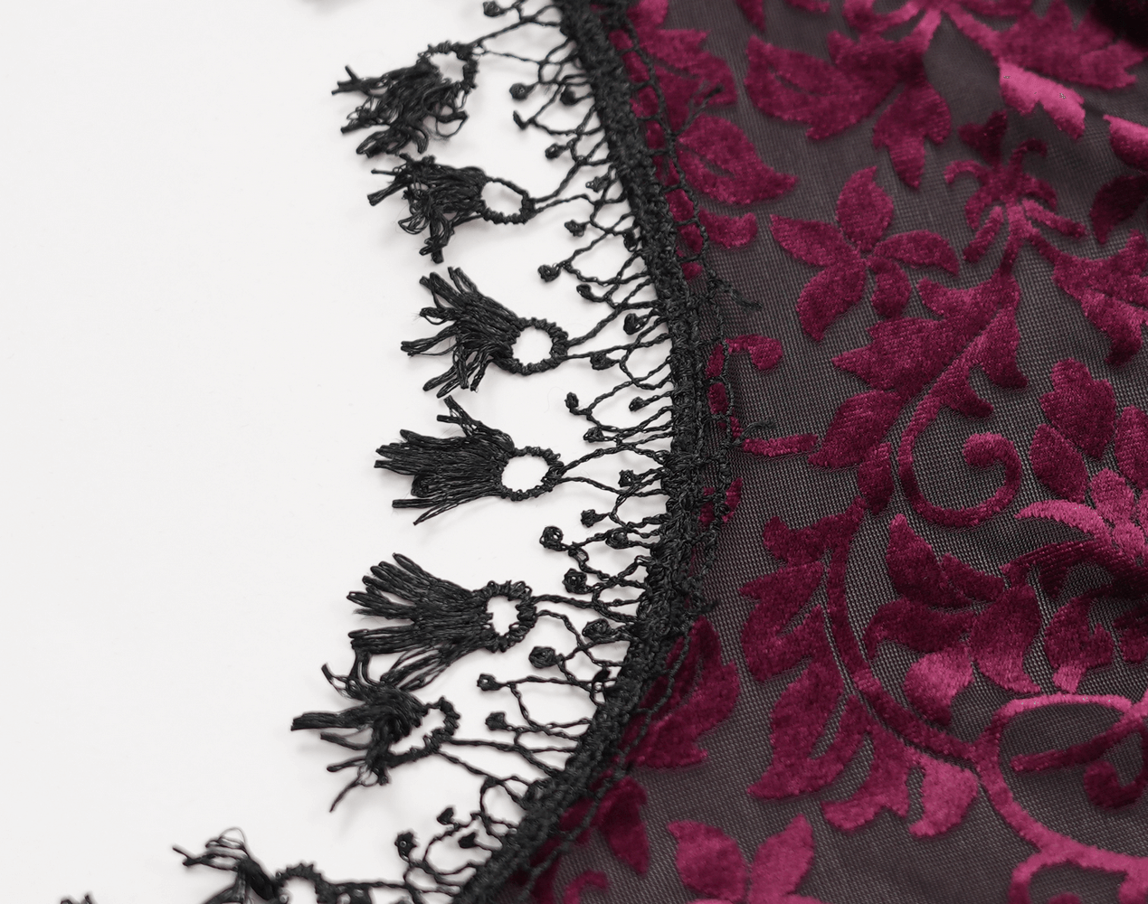 Close-up of burgundy lace fabric featuring intricate floral patterns and delicate black fringe details. Ideal for gothic fashion.