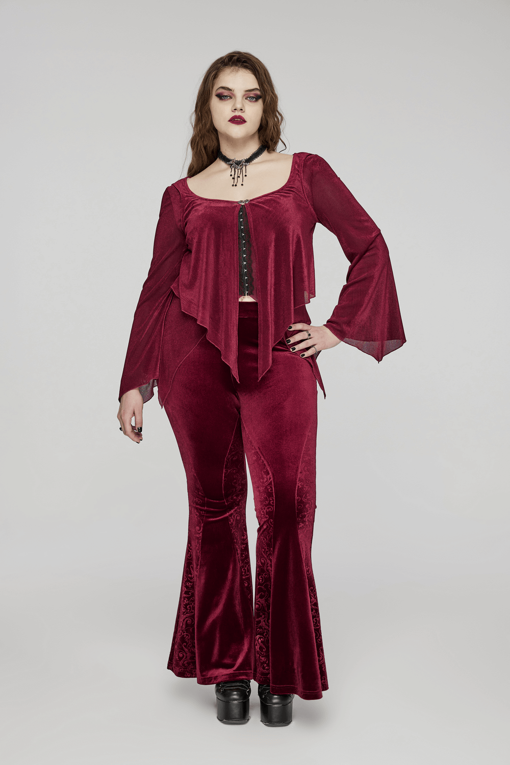 Elegant gothic model in burgundy velvet flared pants with embossed details and stylish bell sleeves.