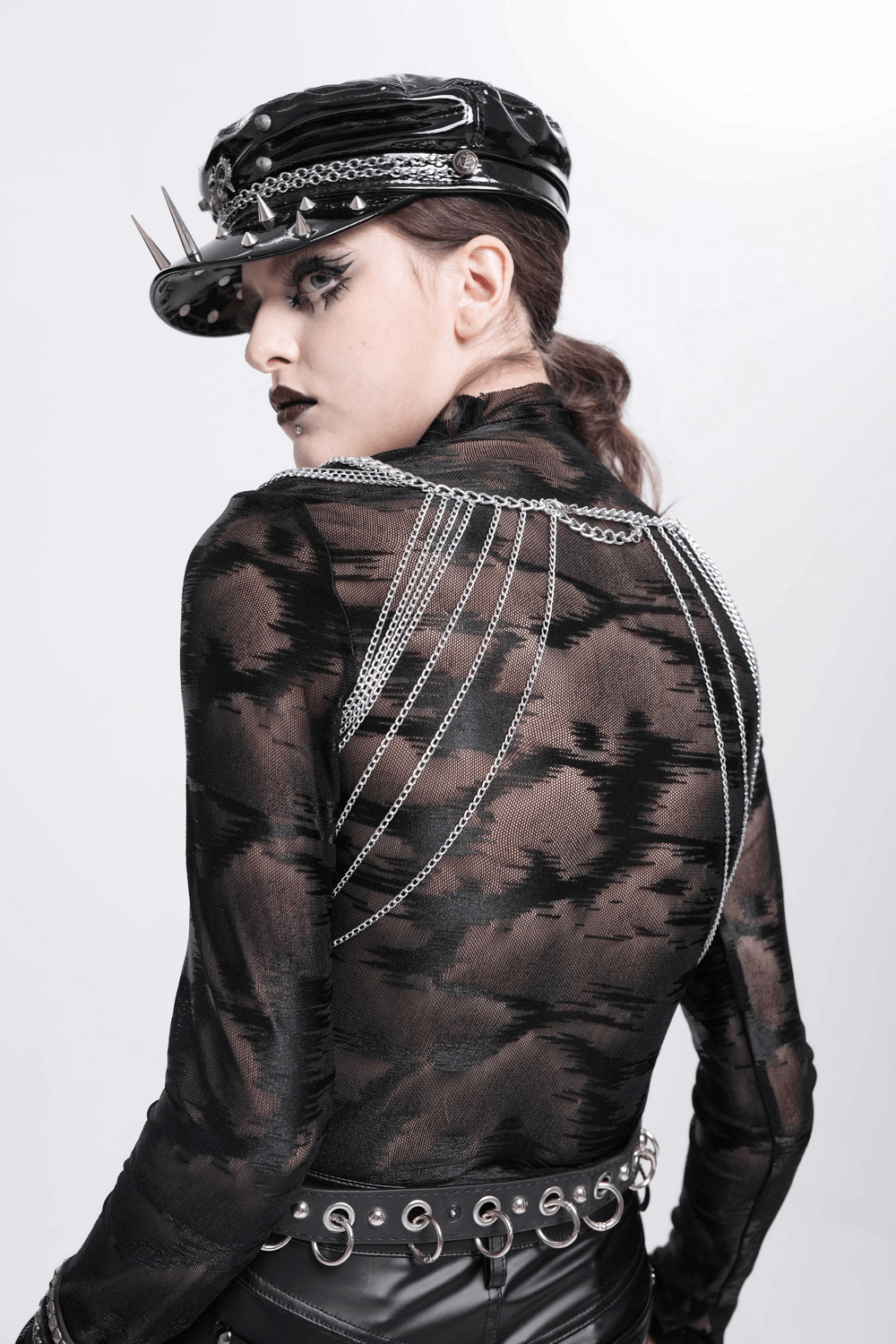 Gothic model showcasing silver hair chain and stylish outfit with spiked hat and edgy accessories.