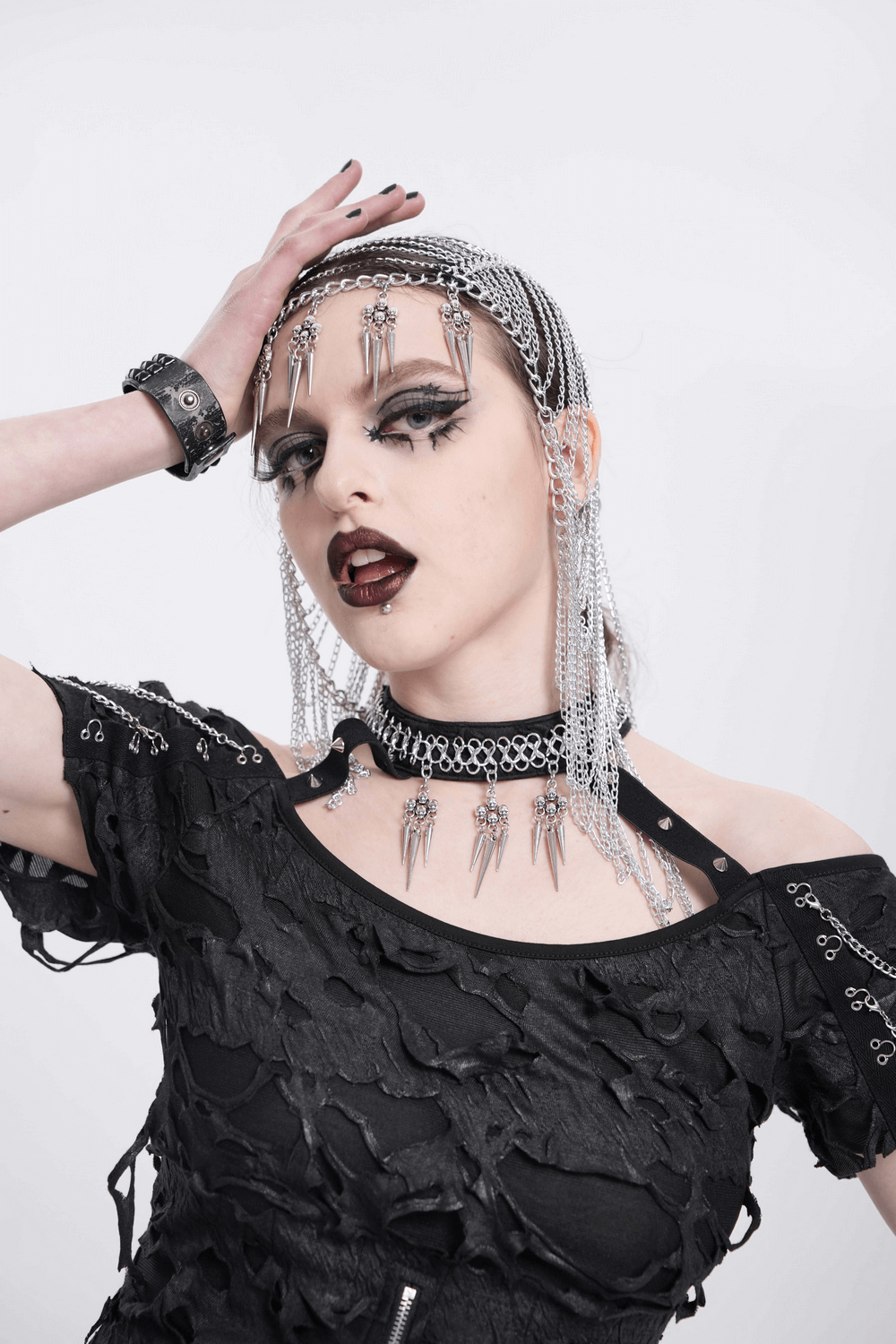 Gothic woman with silver chain headpiece and spiked skulls, showcasing a bold punk aesthetic in edgy black attire.