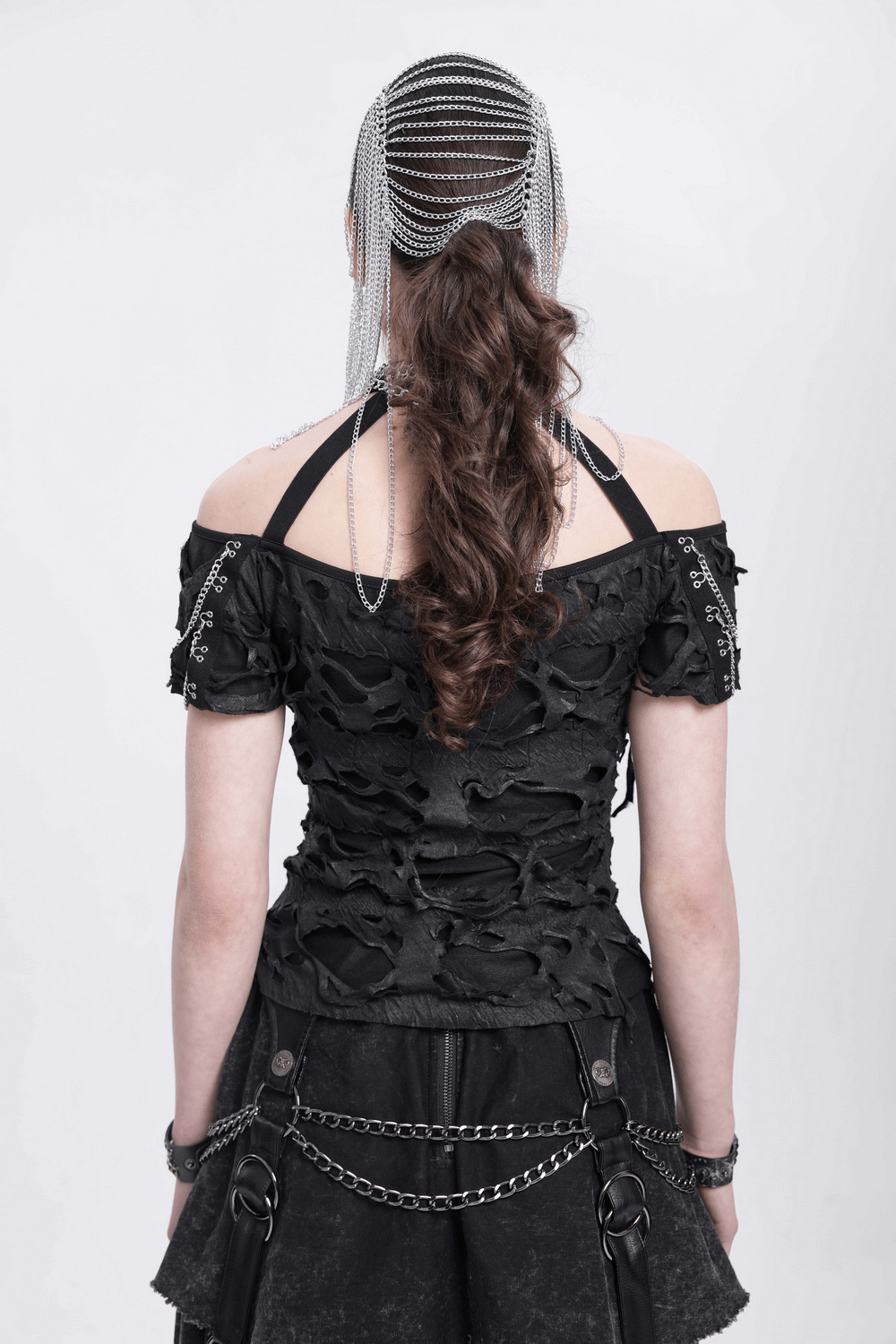 Back view of a model in a gothic outfit wearing a silver chain headpiece highlighting spiked skull details.