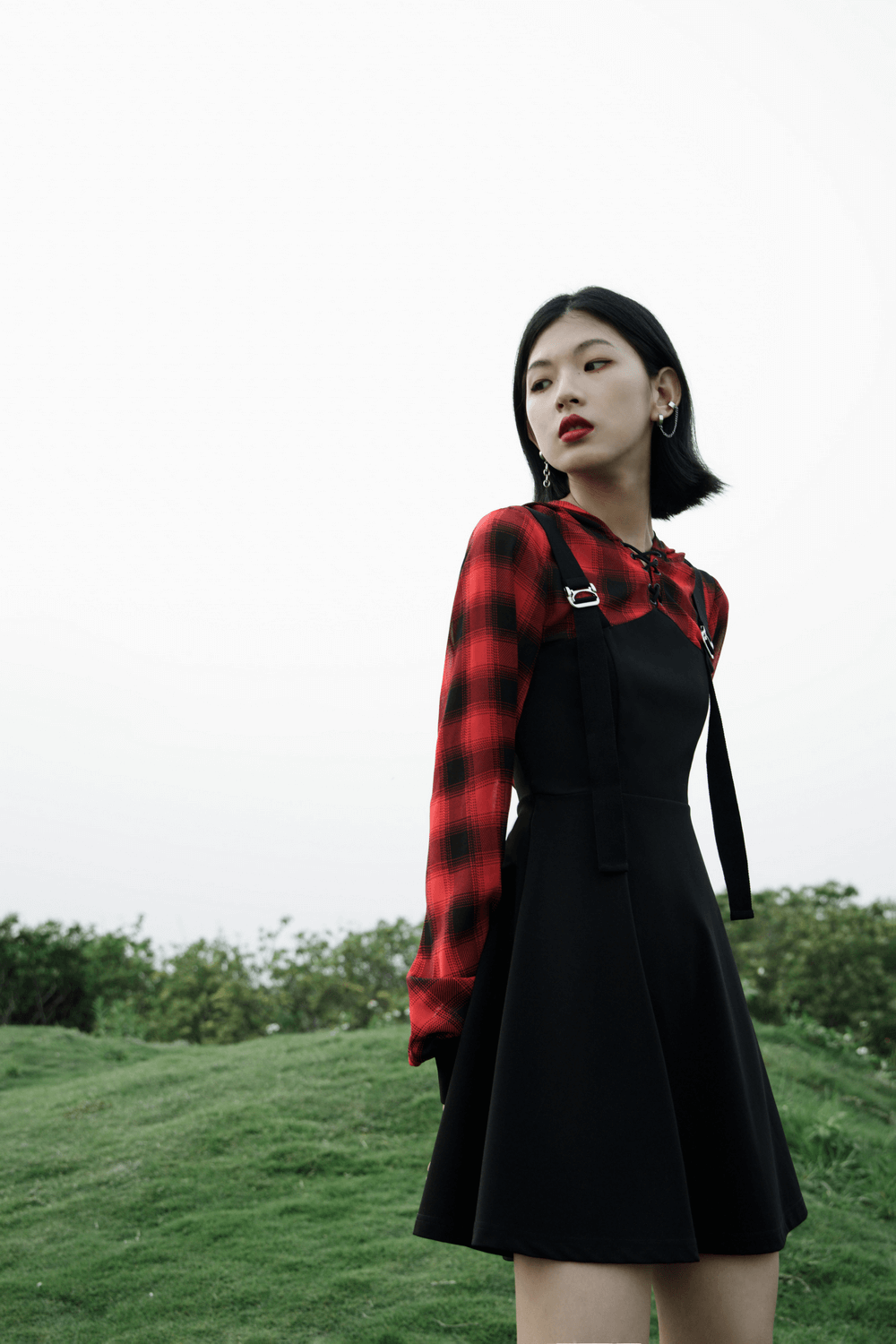 Model wearing a Gothic Chic plaid hooded mini dress with metal buckles against a scenic background.