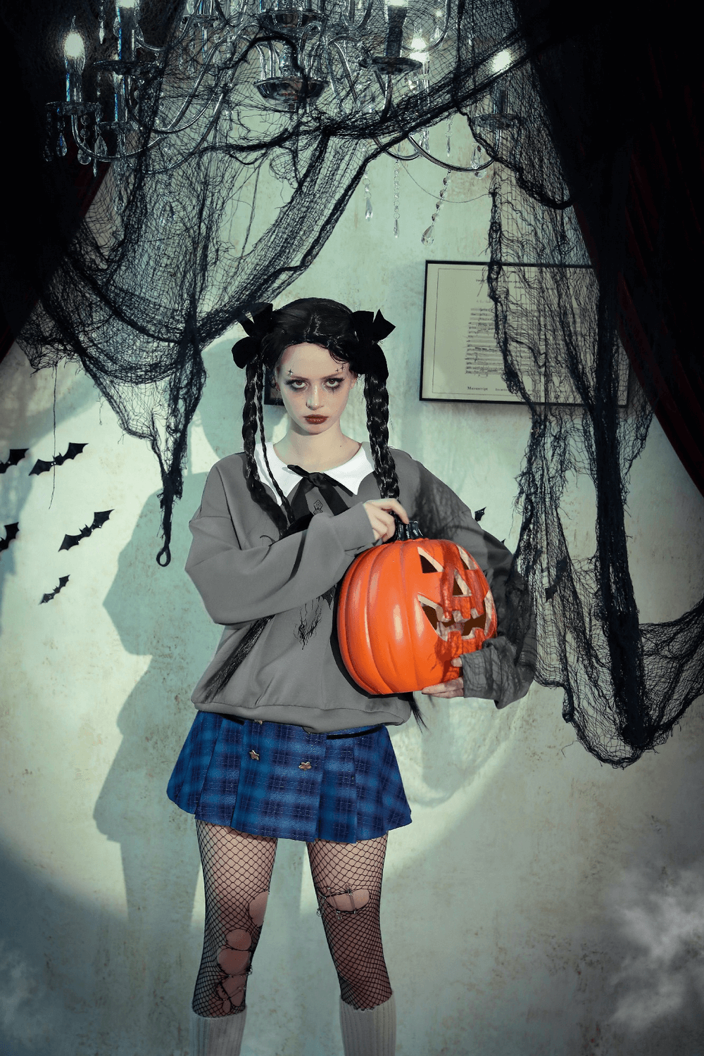 girl in gray sweatshirt holding a carved pumpkin, wearing plaid skirt, surrounded by Halloween decorations and cobwebs.