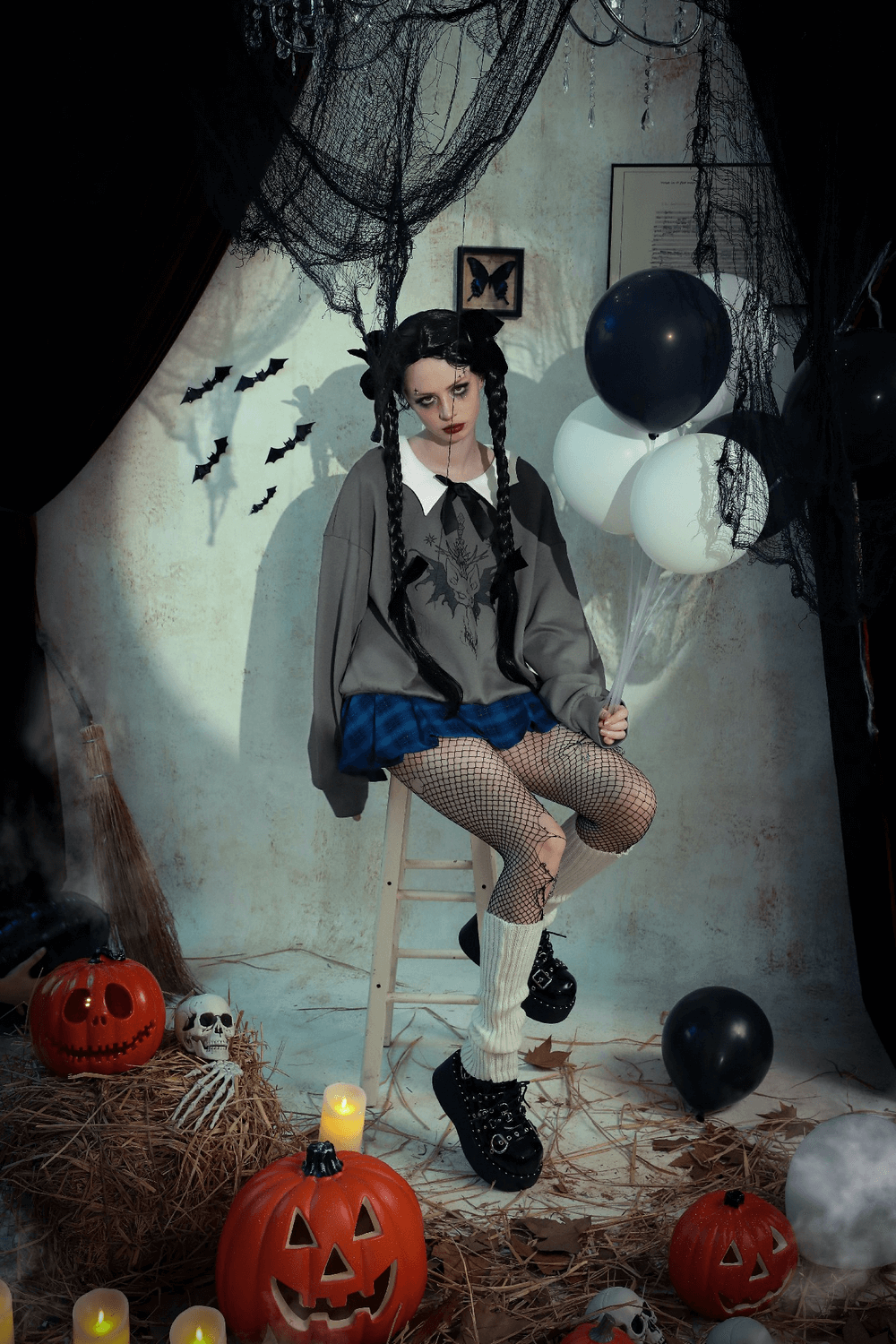 Gothic aesthetic scene with model in dark sweatshirt, fishnet tights, and playful balloons, surrounded by Halloween decor.