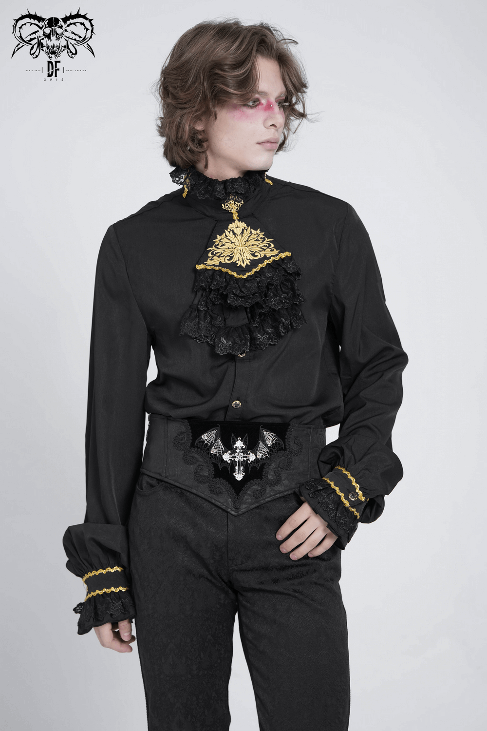 Gothic model in black shirt and corset belt with bat wings and cross embroidery, exuding alternative fashion elegance.