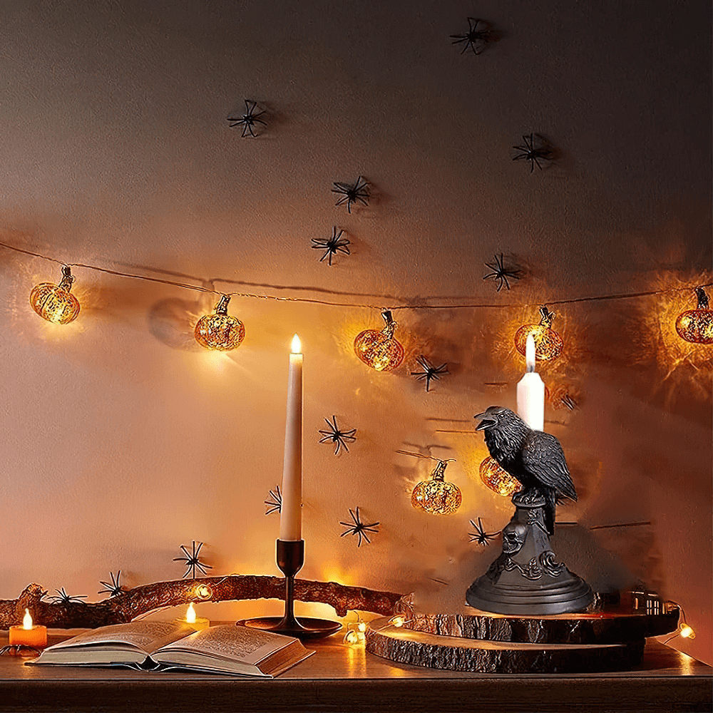 Gothic crow candle holder with skull base surrounded by warm candlelight and decorative pumpkins.