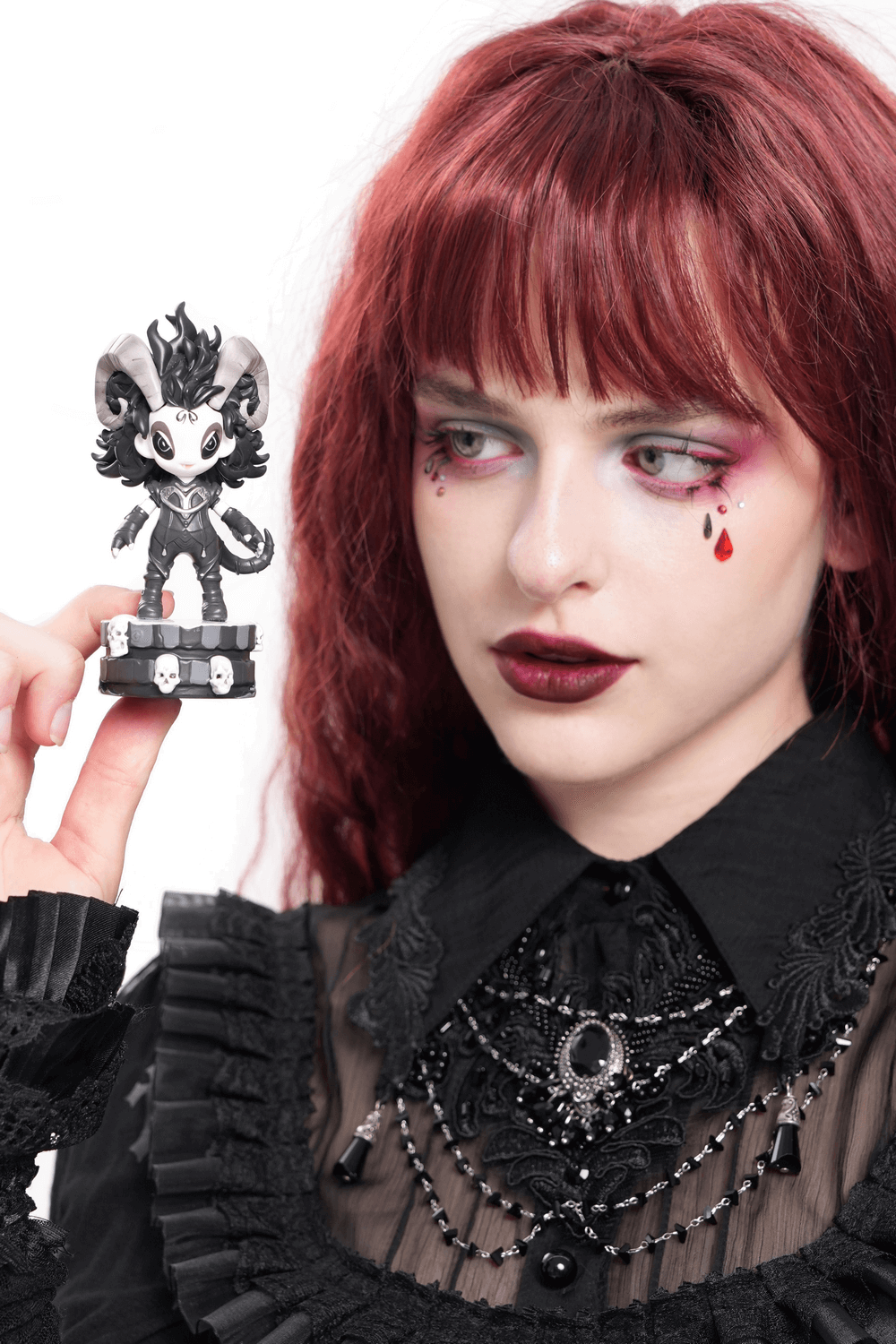 Gothic demon figure with horns held by a dramatic model in dark, elegant attire, showcasing its skull base.
