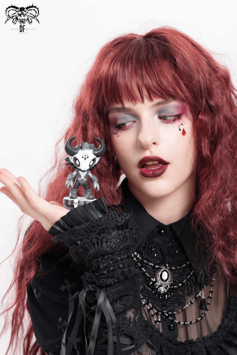 Gothic demon figure with horns held by a model with striking red hair and dark aesthetic.