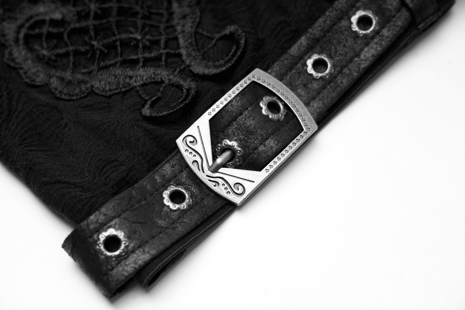 Close-up of a decorative buckle on gothic leg warmers with delicate embroidery, showcasing elegant black fabric.