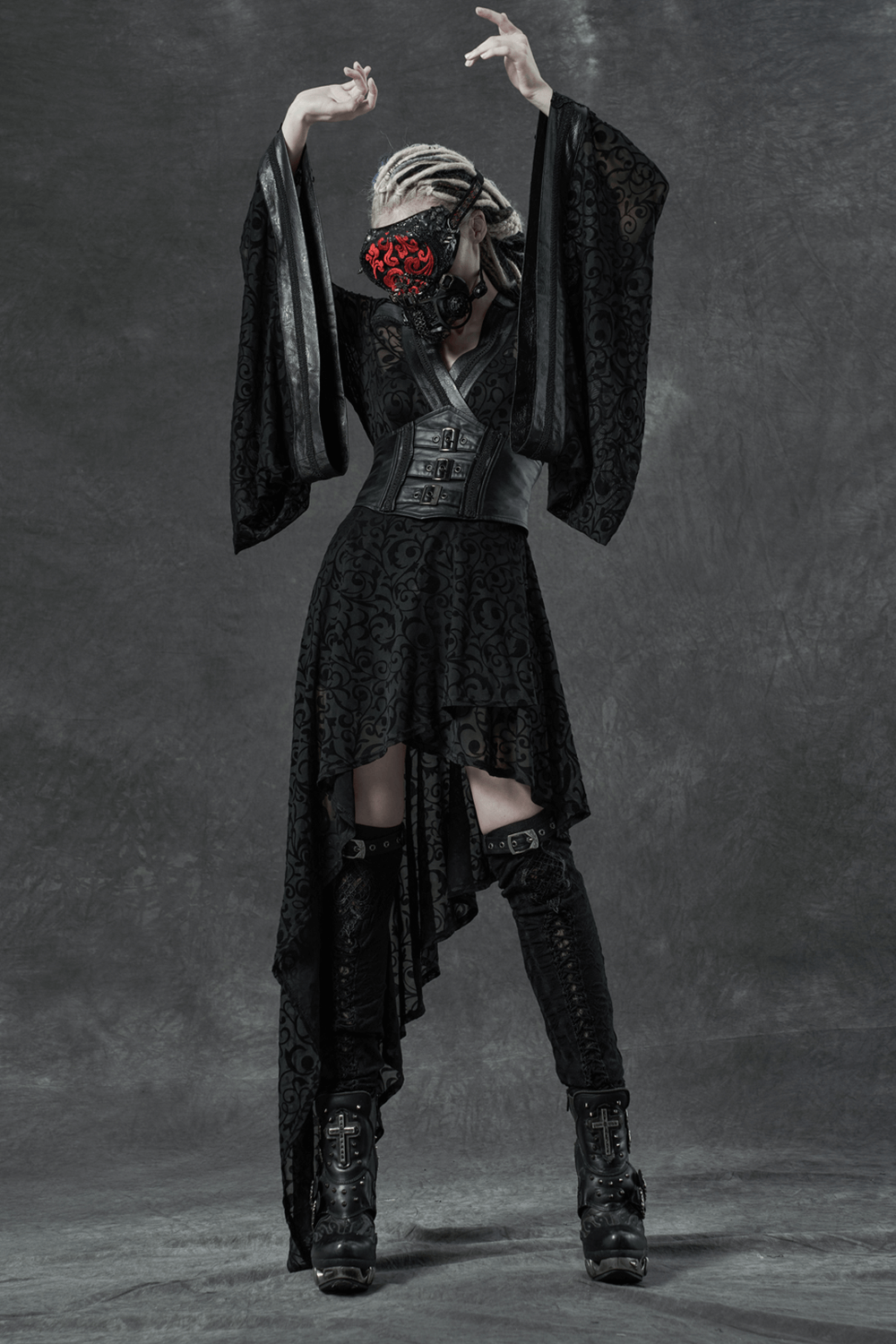 Gothic model showcasing elegant black outfit with flowing sleeves and intricate patterns against a dramatic background.