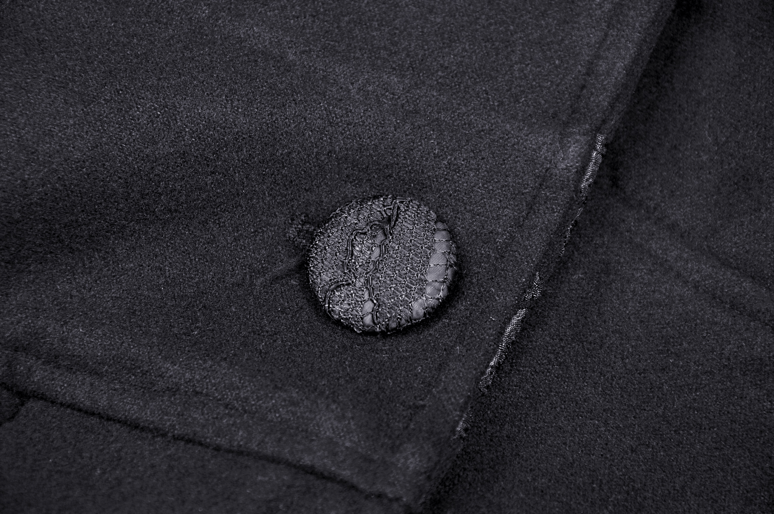Close-up of a textured black button on a gothic female hooded cocktail coat, showcasing its elegant details.