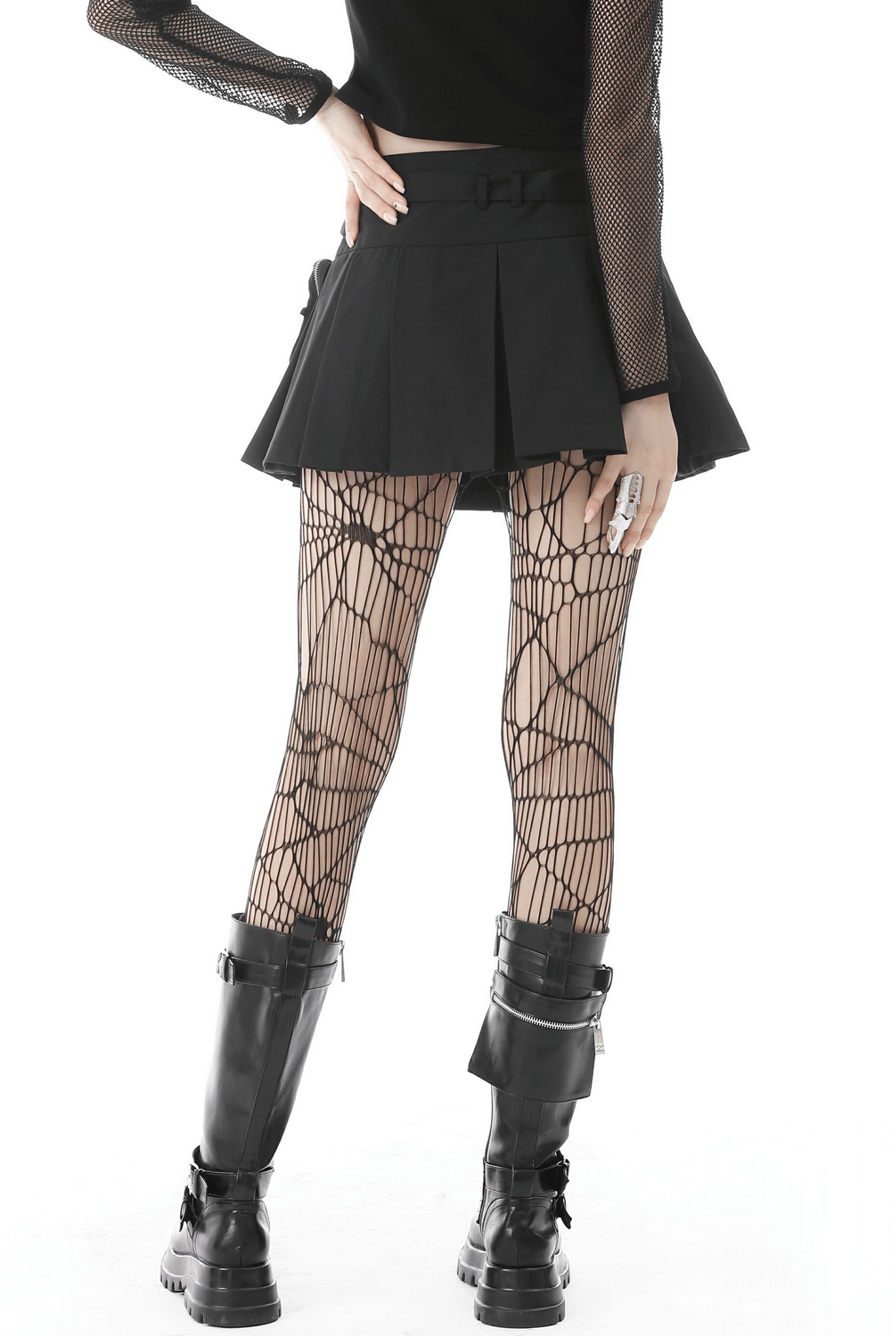 Gothic female model in black pleated mini skirt with chain belt and spiderweb tights, showcasing punk fashion style.