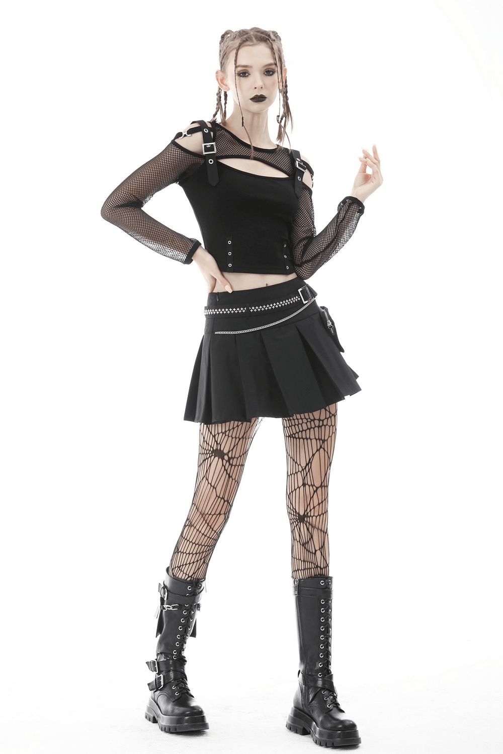 Gothic female model in black pleated mini skirt with chain belt, mesh top, and fishnet tights, showcasing punk style.