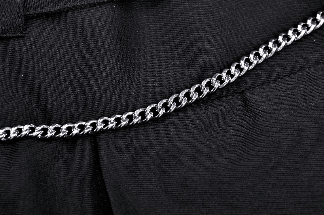 Close-up of a shiny silver chain belt on a black pleated skirt, showcasing dark punk style and edgy fashion.