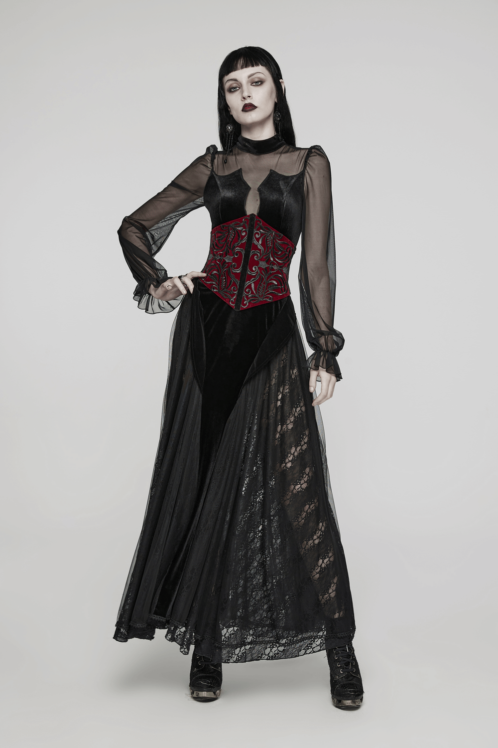 Gothic female model in sheer black dress with deep red velvet corset waistband and floral embroidery.