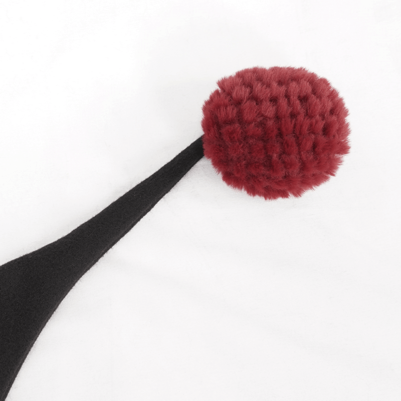 Close-up of a red pompon on a black fabric, showcasing gothic style detail of a women's cape.