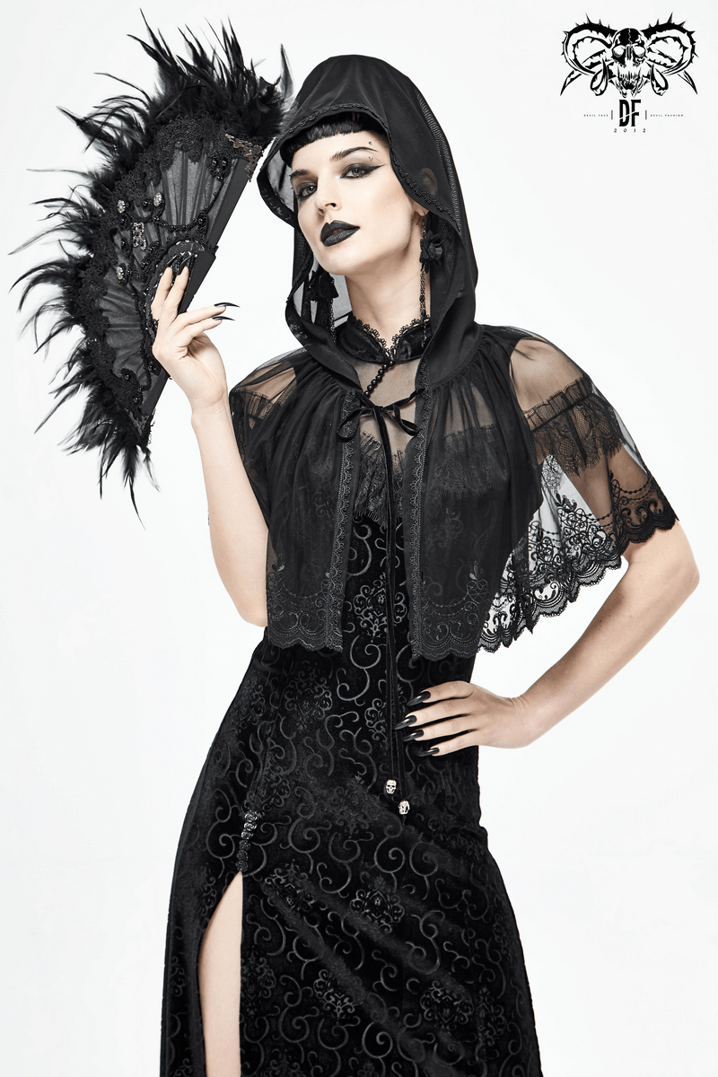 Stylish woman in a gothic black lace cape with hood, holding a black fan, exuding vintage elegance.