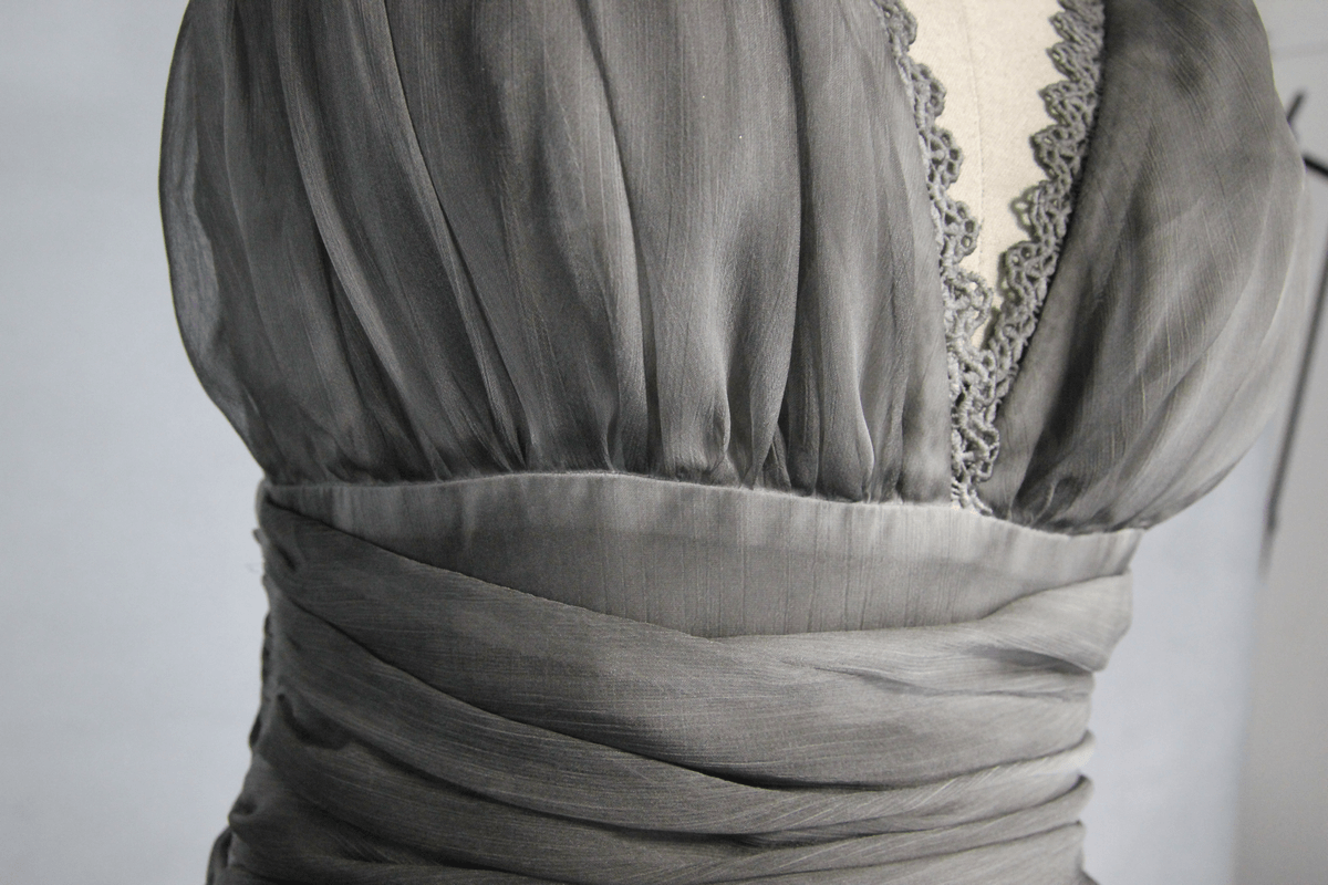 Close-up of a gothic gray women's dress with a deep V neckline and elegant draping, highlighting the backless design.