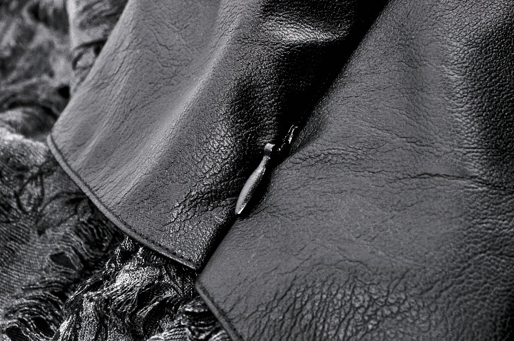 Close-up of black faux leather fabric, showcasing a textured finish and a zipper detail from a Gothic skirt.