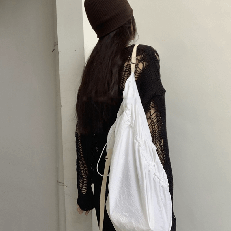 Woman in oversized gothic hollow-out sweater carrying a white bag, showcasing a stylish grunge look.