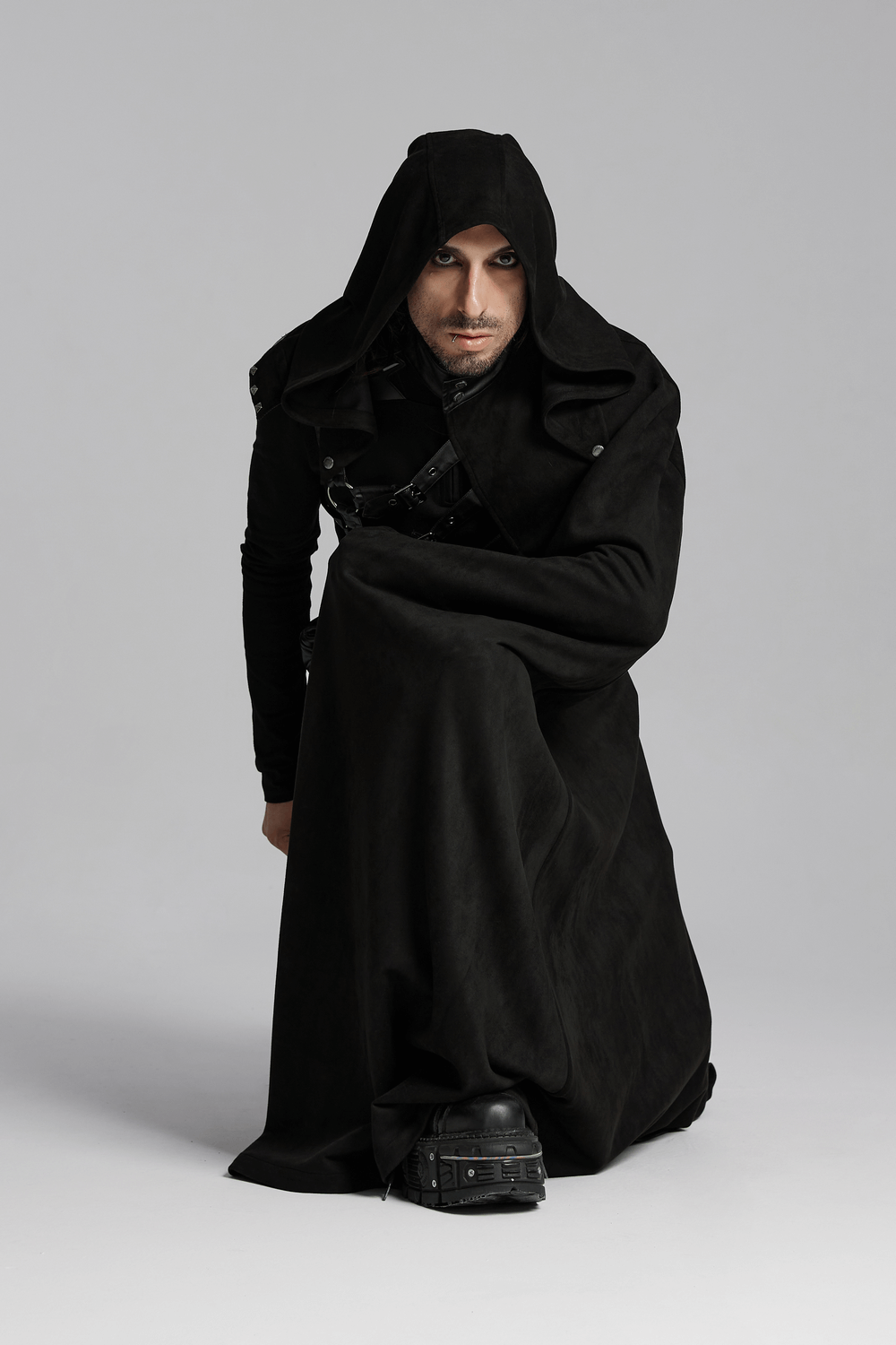 A model wearing a Gothic hooded half cape in black, showcasing an asymmetric design and leather strap details.