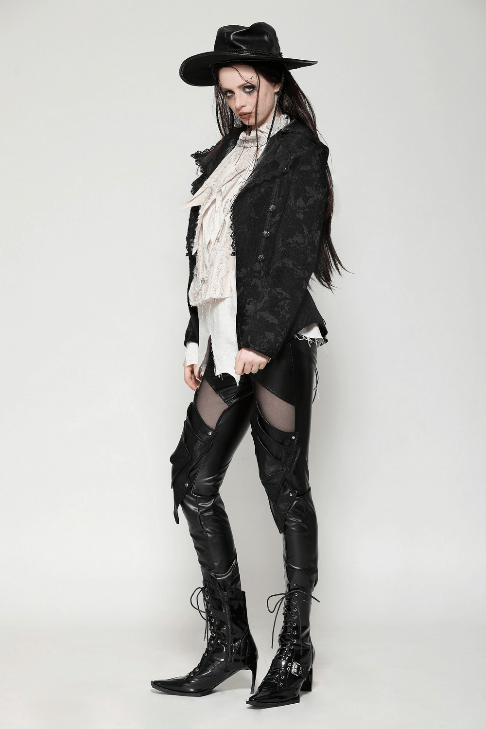 Model showcasing a gothic jacket with lace details, styled with sleek leather pants and a dramatic hat. Perfect for bold fashion statements.