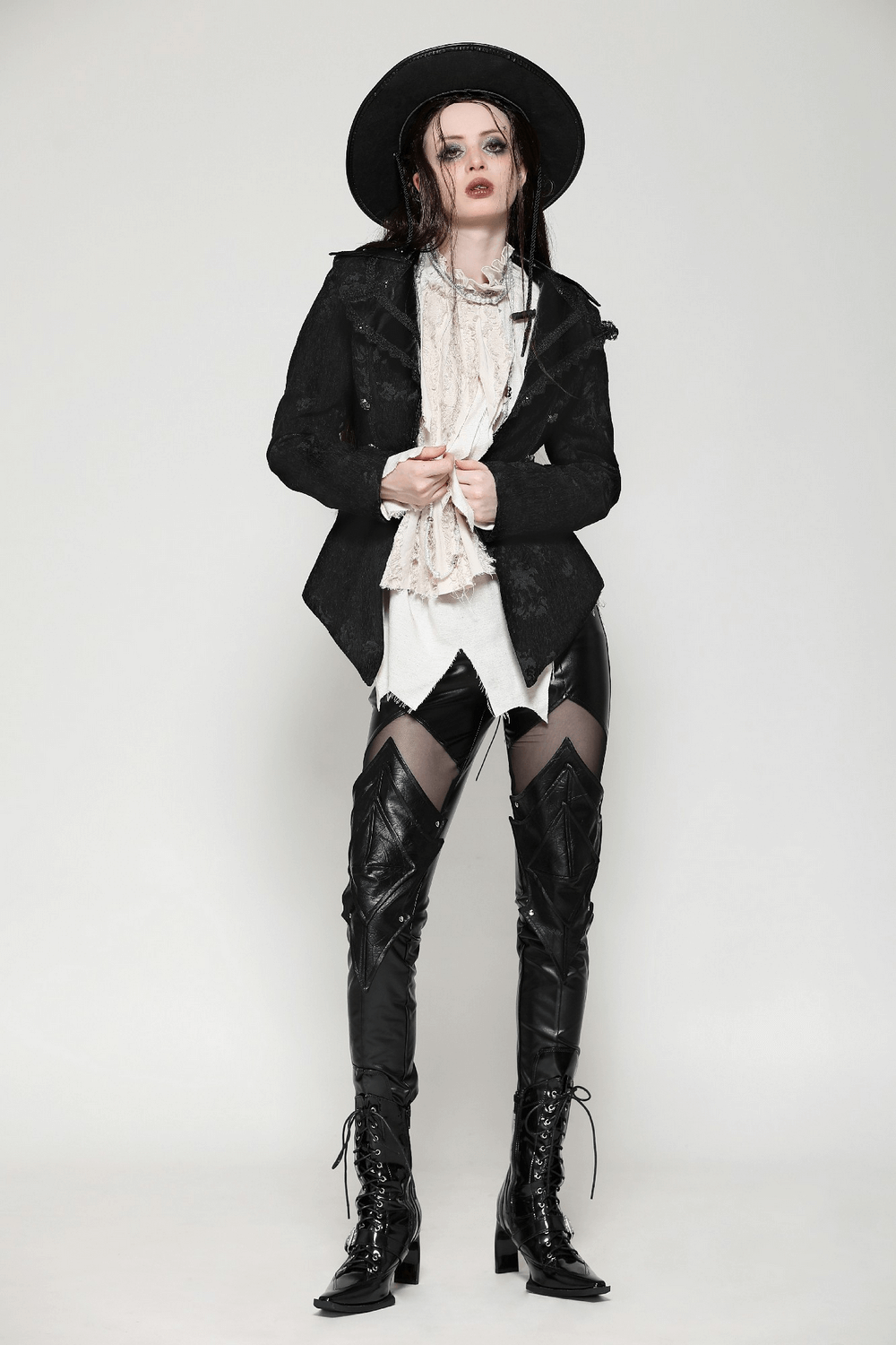 Model in a gothic jacket with lace trim and statement buttons, paired with fitted leather pants and a stylish hat.