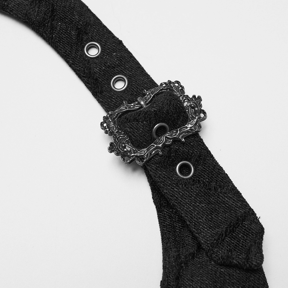 Close-up of ornate antique bronze buckle on black denim vest strap, showcasing gothic fashion details.