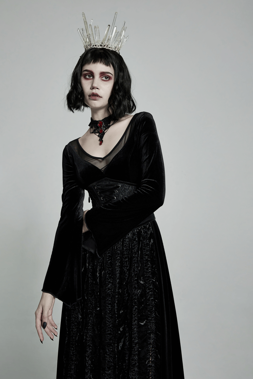 Gothic woman in black velvet dress wearing a crown, showcasing an elegant ruby pendant necklace.