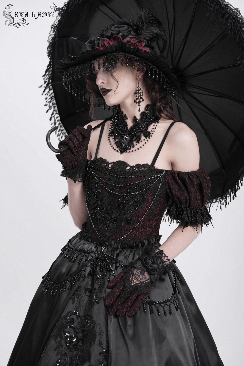 Gothic lace-back maxi dress with chain detail, accessorized with a parasol and elegant jewelry for a stunning look.