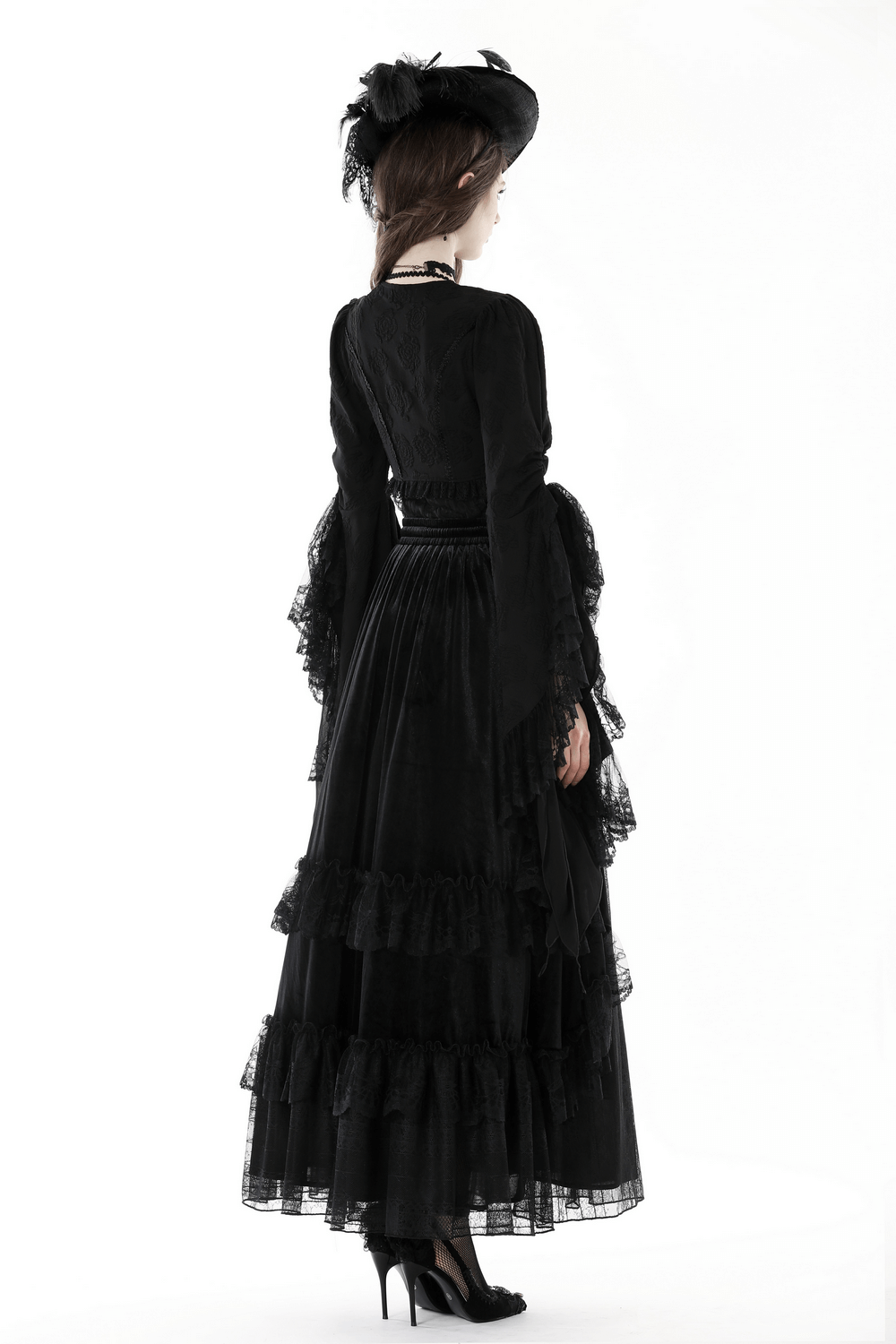 Elegant woman in a black gothic dress with long bell sleeves and ruffled hem, styled with a chic hat.