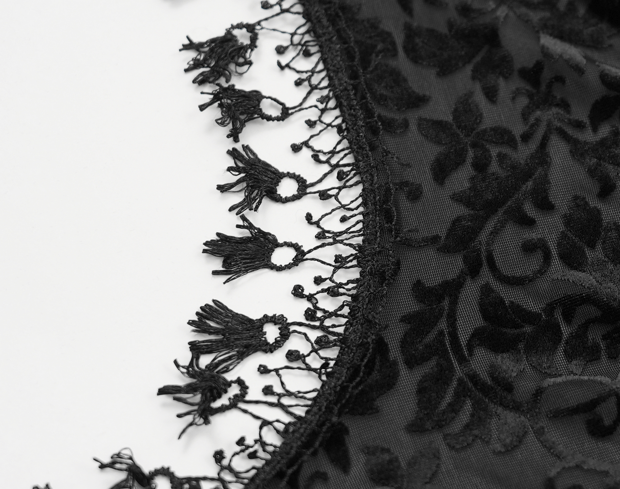 Close-up of intricate black lace detailing with floral patterns and delicate fringe, perfect for gothic fashion.