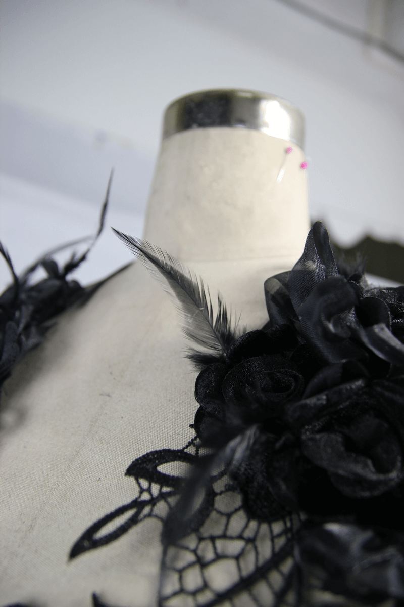 Close-up of a black lace chest harness top with flower appliques on a dress form, showcasing gothic elegance.