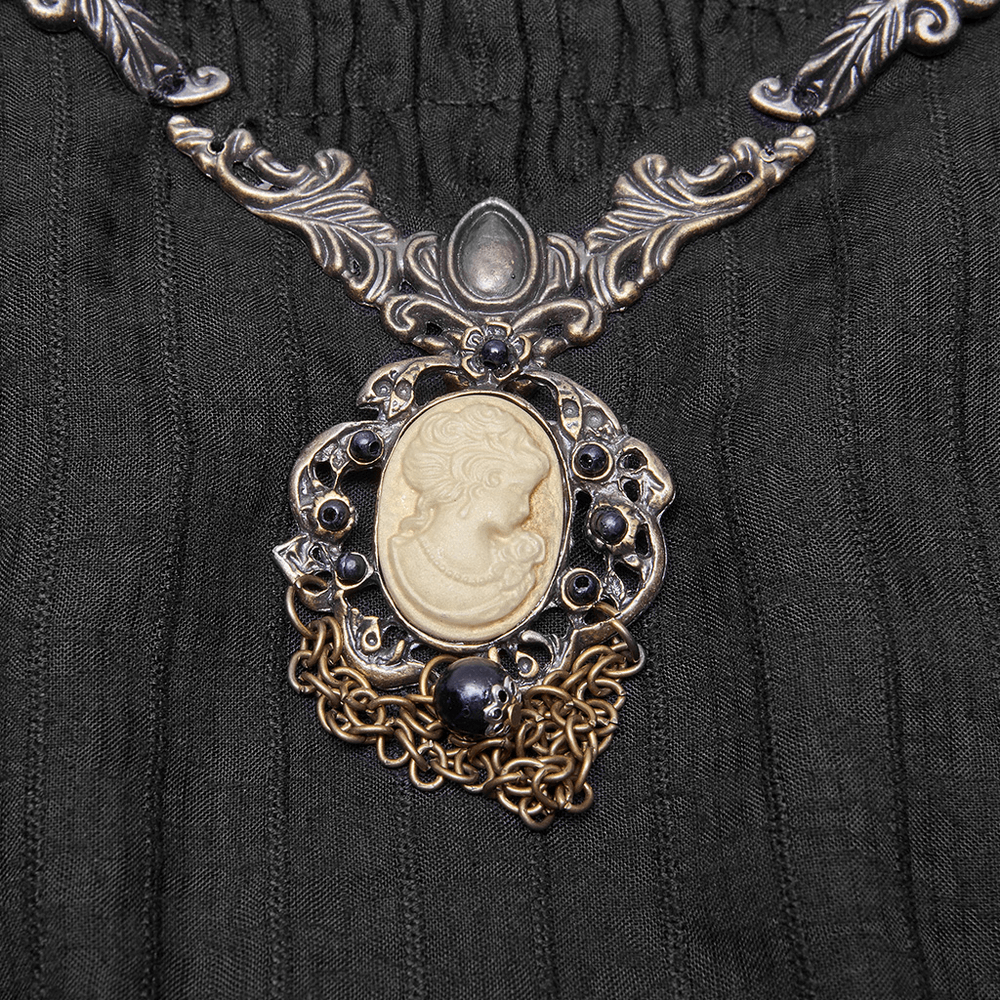 Antique-inspired silver necklace featuring a cameo pendant and intricate chain detailing on a black fabric backdrop.