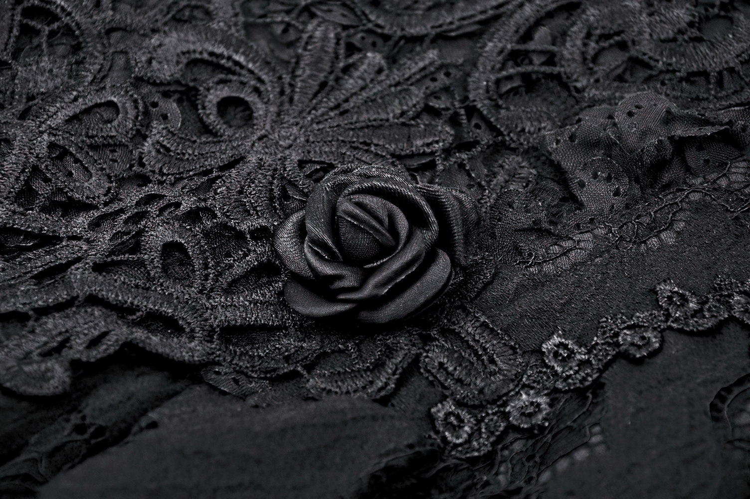 Close-up of black lace fabric with intricate patterns and a decorative black rose, perfect for gothic fashion.
