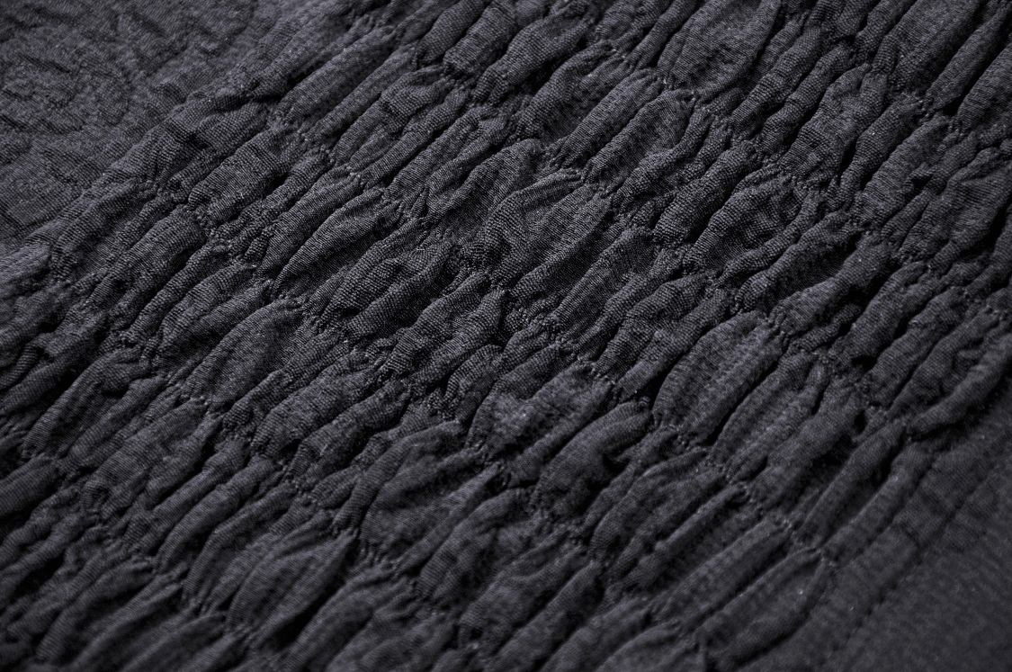 Close-up of intricate smocked fabric detail in dark Gothic lace for a high-low halter dress, showcasing craftsmanship.