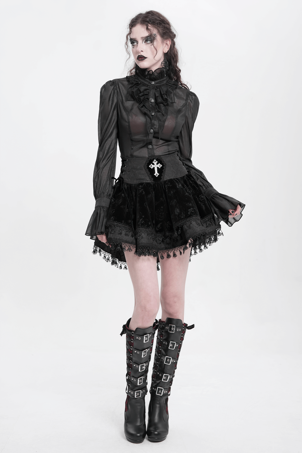 Gothic model in black lace-up velvet skirt with cross embellishment and statement boots, showcasing Victorian style.