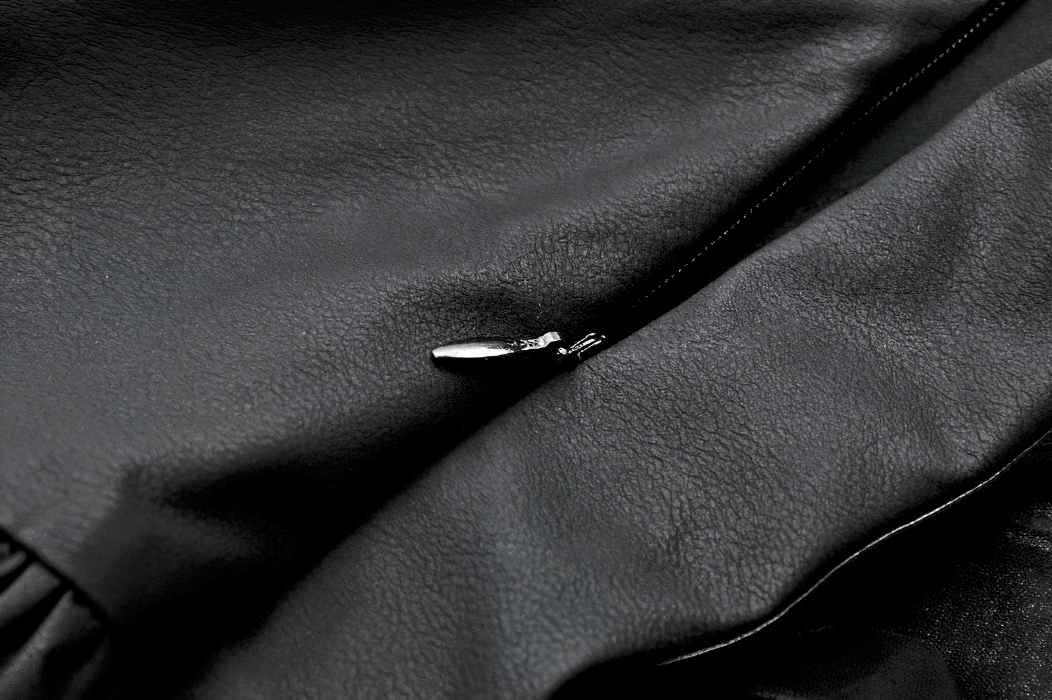 Close-up of black leather fabric with zipper detail, showcasing texture and design elements.