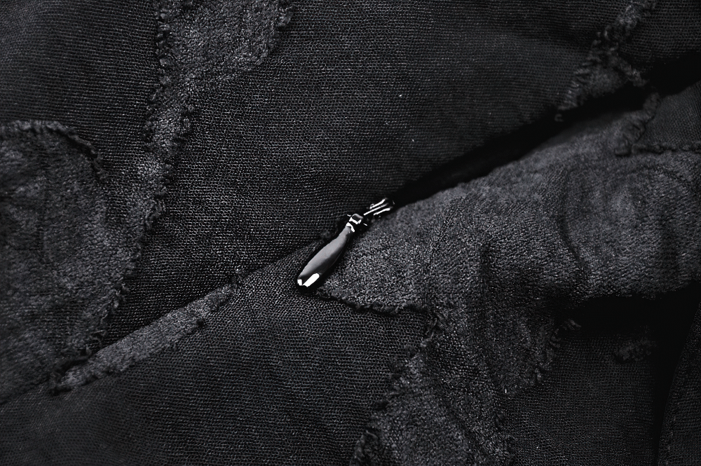 Close-up of black fabric featuring intricate textures and a small zipper detail, highlighting Gothic fashion elements.