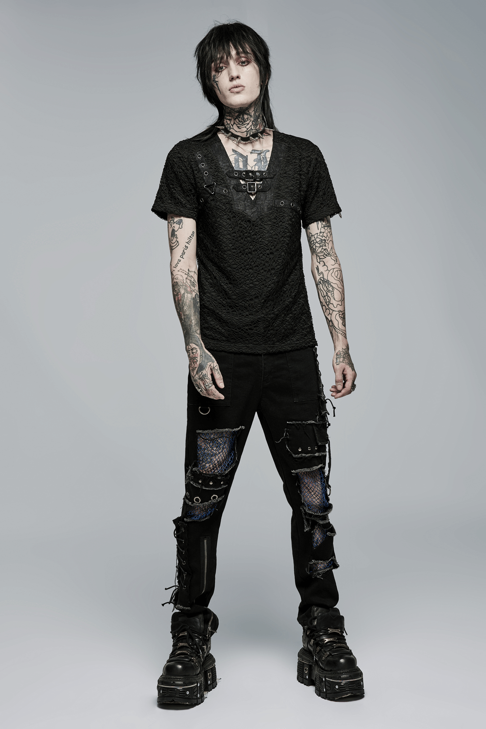 Stylish gothic male model in a black lace-up mesh V-neck tee and edgy distressed pants, showcasing rebel elegance.