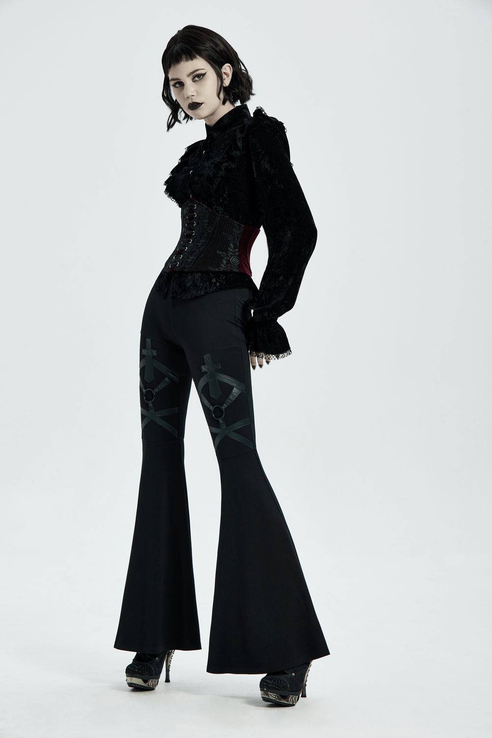 Gothic lace-up velvet corset with red accents paired with stylish black flared pants in a hauntingly elegant pose.