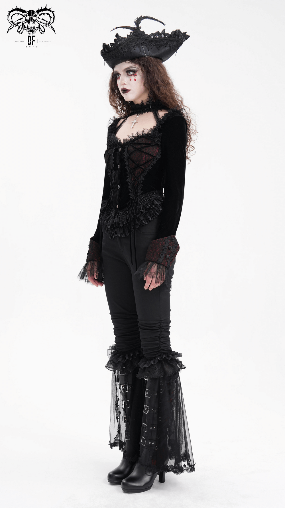 Gothic women's long-sleeved top with lace-up front and ruffle sleeves, paired with stylish black pants and dramatic hat.