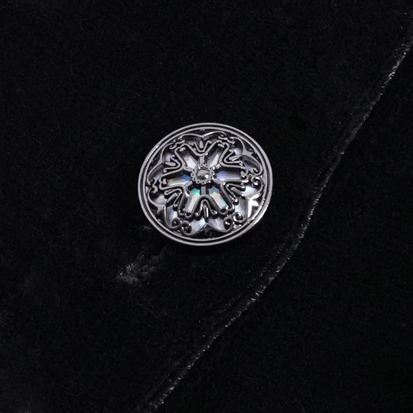 Close-up of an ornate silver button with intricate design on a black fabric background.